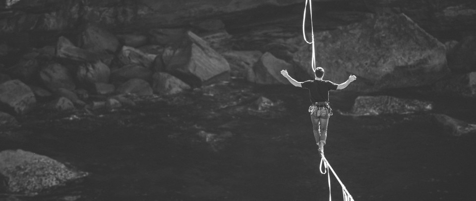 Person walking on tightrope. There are rocks and water below.